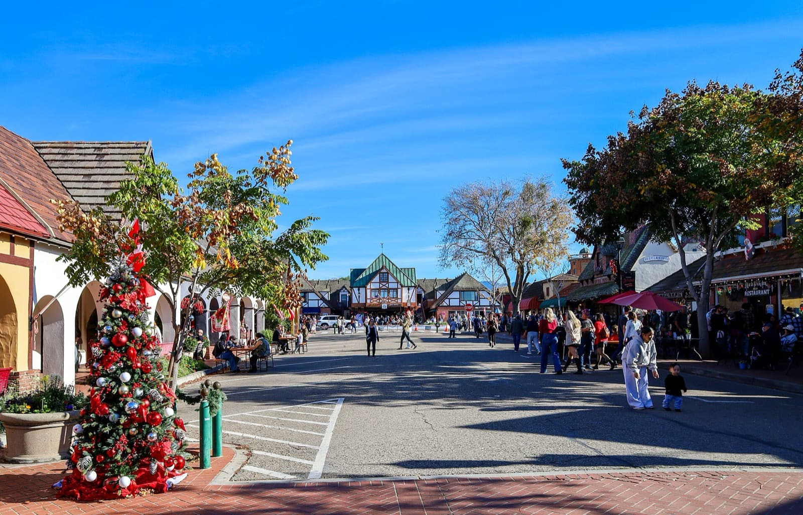 Visitors walking through the pedestrian plaza in downtown Solvang, California, with Danish half-timbered buildings and a Christmas tree
